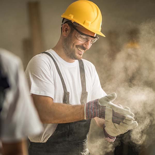 Young happy worker cleaning sawdust from his protective gloves at construction site.